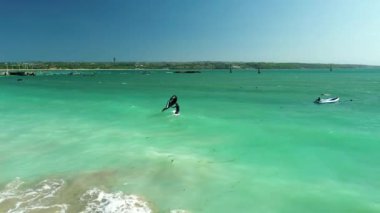 Bir erkek uçurtma sörfçüsünün, yelkeni sörf tahtasına yayıp okyanusun turkuaz suyuna bindiği hava görüntüsü. Rüzgarlı havada aşırı bir spor. Bali 'de uçurtma sörfü.