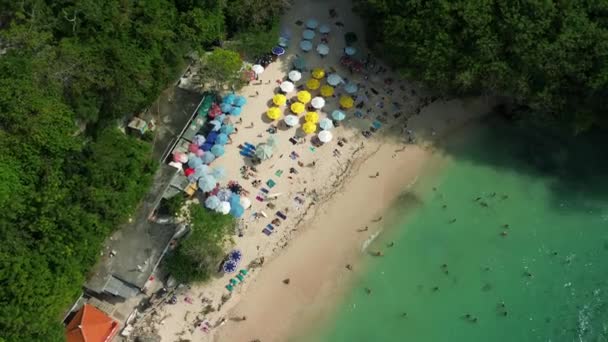 鸟瞰完美的海滩 为游客提供五彩缤纷的雨伞和日光浴 旁边是碧绿的海洋和悬崖 在热带岛屿上的天堂里放松 在拥挤的海滩上放松 — 图库视频影像