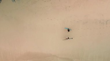 Spor bikinili iki genç sörfçü kızın ellerinde sörf tahtalarıyla okyanus kenarındaki beyaz bir plajda yürüyüp dalgalara baktığı hava manzarası. Sörf topluluğu.