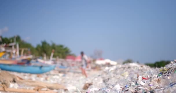 一个被塑料垃圾污染的海滩的特写镜头 一个男人从后面走过 全球环境灾难 海滩上堆积如山的垃圾来自海洋 拯救地球 — 图库视频影像