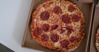 İçinde pepperonili pizza olan bir karton kutunun olduğu bir masanın üst görüntüsü. Çerçevede bir erkek eli belirir ve bir dilim pizza alır. Bütün pizzayı tek başına ye. Pizza teslimatı..