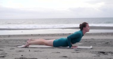 Siyah kumlu plajda spor giyinen genç bir kadın yoga yapıyor. Konsantre ve sakin. Dalgaların sesine göre esneme ve meditasyon. Vücuduna bakıyorum. Yaz yaşam tarzı.