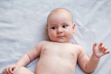 4 aylık beyaz bir bebeğin portresi açık bir battaniyenin üzerinde çıplak bir şekilde bez bağlayıp yukarı bakıyor. Küçük bir kız şaşkınlıkla etrafına bakıyor, yeni doğmuş bir bebeğin duyguları. Anneler Günü.