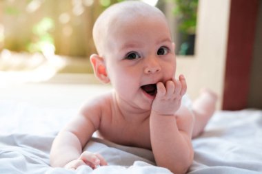 Bebek yazın bahçede hafif bir battaniyeye uzanmış elini çiğniyor ve gülümsüyor. İlk dişler kesiliyor, bebek diş etleri kaşınıyor. Doğada küçük mutlu bir kız.