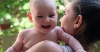 Genç bir kadın, evinin arka bahçesinde kucağında bir bebek tutuyor. Yeni doğmuş küçük bir kız annesinin kollarında gülüyor ve doğayı dikkatlice inceliyor. Anneler Günü.
