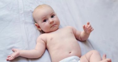 Bebek bezli bir bebek battaniyeye uzanıp gülüyor, annesi kollarını ve bacaklarını kaldırıyor, ısınıyor ve jimnastik yapıyor. Yeni doğan bebeğin bakımı ve sağlığı, çocuk için egzersizler. Anneler Günü.