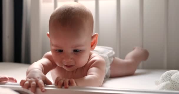 面白い赤ちゃんは小さな手でベッドの側面を保持し ベビーベッドを動かすように強制しようとします 生まれたばかりの赤ちゃんのおかしい顔 母性の幸せ マザーズ — ストック動画