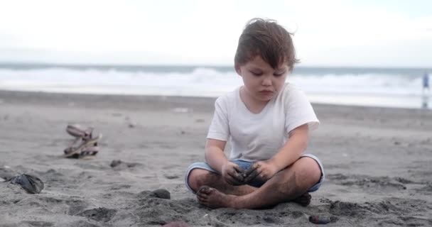 Маленький Хлопчик Грає Чорному Піщаному Пляжі Біля Океану Він Зосереджений — стокове відео