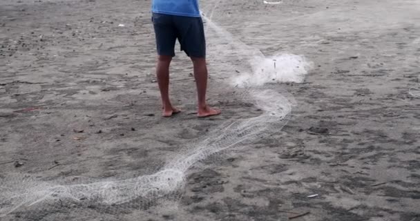 漁網を集めて修理する黒いビーチの漁師の足の様子 漁師として働く中年のアジア人男性が 砂の上に網を広げました 認識できない人 — ストック動画