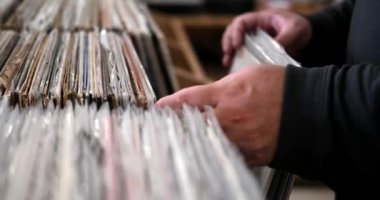Samimi bir vinil mağazasından geniş bir plağın plağını seçen bir adamın yakın çekimi. Analog ses olarak klasik ve rock müzik. Müziksever, eski bir marketten alışveriş yapıyor..