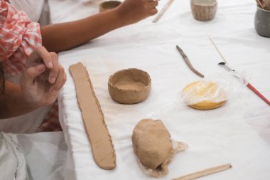 Önlükle bir sanat atölyesinde oturup çömlek kilinden kupa yapan iki farklı beyaz ve Afrikalı kadının yakın çekimi. Topraktan bir kap oluşturup iletişim kuruyorlar..