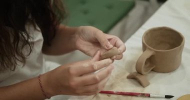 Bir kupayı süslemek için kilden kalbi şekillendiren genç bir kadının yakın çekimi. Yaratıcı bir atölyede yüksek lisans dersi. Sevgililer Günü yaratıcı hobileri.