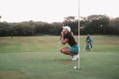 Acemi bir golfçü olan genç bir kadın golf sahasında çömeliyor ve elinde bir sopa tutuyor. O, deliği kaçırdığı ve rekabeti kaybettiği için üzgün. Yenilgiden dolayı hayal kırıklığı.