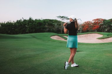 Genç bir kadının golf sopasıyla topa vurup vurmadığını görmek için topa vurup vurmadığını görmek için uzaklığa bakıyor. Golf kulübünde profesyonel golf. Yaz sporu.