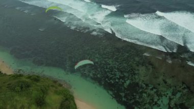 Bali 'de okyanus ve uçurum kenarında yamaç paraşütü yapan bir grup insanın hava görüntüsü. Turistler için aşırı boş zaman. Deniz kenarında paraşütle uçmak, sahilin manzarası. Yaz tatili.