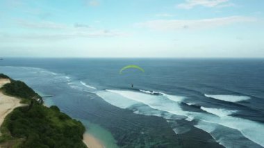 Bali 'de okyanus ve uçurum kenarında yamaç paraşütü yapan bir grup insanın hava görüntüsü. Turistler için aşırı boş zaman. Deniz kenarında paraşütle uçmak, sahilin manzarası. Yaz tatili.