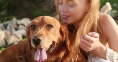 Plajda altın av köpeğinin yanında çilli genç kızıl saçlı bir kadının portresi ve onu başından öpmesi. Sadık köpeğinle yaz tatili. Okyanus kıyısında şafak.