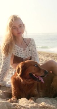 Dikey, genç kızıl saçlı kadın ve onun golden retriever 'ı gün doğumunda okyanusun arka planında oturuyorlar. Bir kadın köpeğini okşar, uzaklara bakar ve tatilin tadını çıkarır.