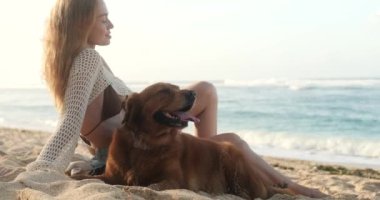 Genç kızıl saçlı bir kadın ve onun golden retriever 'ı gün doğumunda okyanusun arka planında oturuyorlar. Bir kadın köpeğini okşar ve uzaklara bakar, gülümser ve tatilden zevk alır.