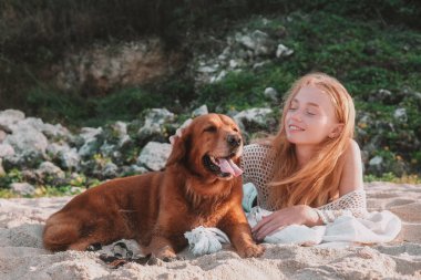 Plajda Golden Retriever köpeğinin yanında yatan genç kızıl saçlı kadın. Köpeği okşar ve ona sevgiyle bakar. Tropik bir adada evcil hayvanınla yaz tatili.