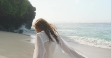 Bikini ve şeffaf açık tişörtlü çekici kızıl saçlı bir kadın okyanus kıyısındaki kumlu bir sahilde dönüyor ve mutlu bir şekilde gülüyor. Uzun zamandır beklenen yaz tatili. Kumsalda bir sabah.