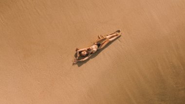Bikini giymiş, kumsalda altın kumu olan ve güneşlenirken güneşlenen genç ve seksi bir kadın. Tüy dökümünden sonra pürüzsüz cilt. Yaz tatili kavramı.