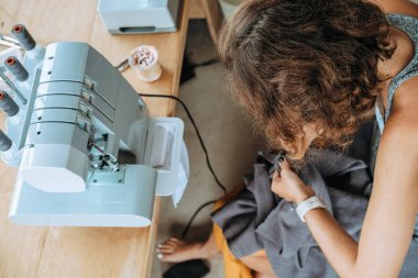 Dikiş makinesine hafif kumaştan pantolon dikebilen genç bir terzinin ellerinin üst görüntüsü. Bir makineye dikiş atar ve işlemi kontrol eder. Küçük başlangıç stüdyosu.