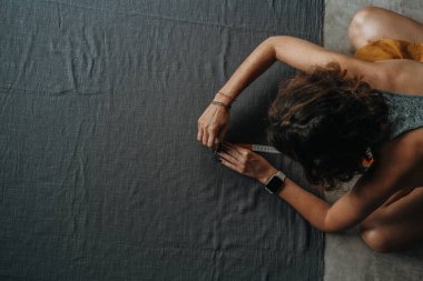 Önünde, yerde oturan bir kadının en üst görüntüsü büyük gri bir kumaş parçası ve onu makasla kesiyor. Bir terzi, müşterisine elbise dikmek için kumaş hazırlar..