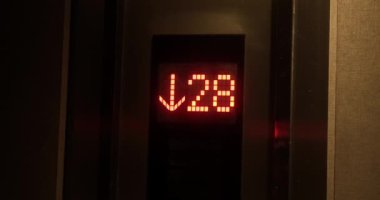 Asansörde zemin geri sayımı ve kırmızı sayıları olan bir elektronik panoya yakın çekim. Asansörden in, tahtadaki ok yanıp sönüyor ve yönü gösteriyor..