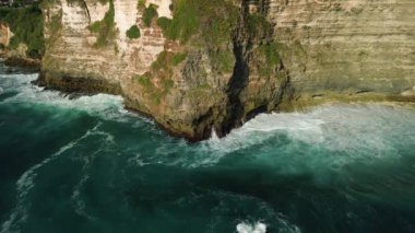 Hint Okyanusu kıyısındaki Bali adasındaki yüksek bir kayanın havadan görünüşü. Büyük dalgalar kayalara çarpıyor, sıçramalar ve köpükler yaratıyor. Arkaplan doğal video.