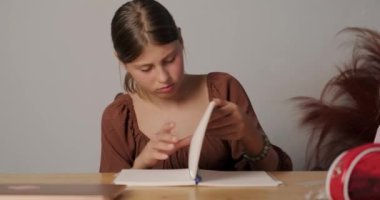Genç kız evdeki masasında oturmuş ödevini yapıyor. Notunu defterinde kaybetmiş ve kaşlarını çatmasını bekliyor. Liseye hazırlanıyorum. Okula geri dön..