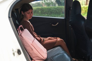 Yanında okul çantasıyla arabanın arka koltuğunda oturan genç bir kız. Çocuk ne yazık ki okul çantasına bakıyor. Annem yaz tatilinden sonra kızını okula getirdi. Okula geri dön..