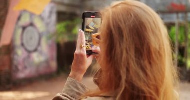 Açık hava iç tasarım sergisinde telefonuyla fotoğraf çeken kızıl saçlı genç bir kadının arkasından yaklaş. Yeni şeyler öğrenmek ve kültürlü bir insanın yaşam tarzı..