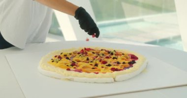 Pavlova düğün pastasını taze çilekle süsleyen kadın pasta şefinin ellerini kapatın. Kremalı pasta tabakasının üstüne çilek serpiyor. Şölen salonunda parti için modaya uygun bir pasta.