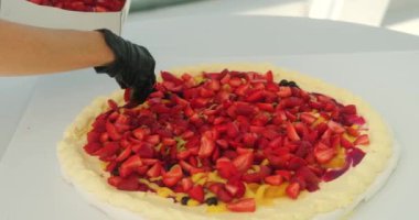 Pavlova düğün pastasını taze çilekle süsleyen kadın pasta şefinin ellerini kapatın. Kremalı pasta tabakasının üstüne çilek serpiyor. Şölen salonunda parti için modaya uygun bir pasta.