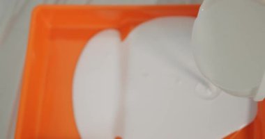 Plastik tepsiye dökülen bir evin içindeki duvarlar için beyaz akrilik boya yakın plan. Yeni bir evin yenilenmesi, duvarların boyanması. Sıvı boya akar ve damla oluşturur. Tasarım ve yaratıcılık.