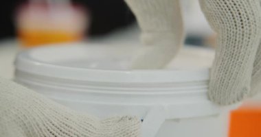 İnşaat eldivenli bir adamın beyaz boya kutusunu açtığı yakın çekim görüntüsü. Evin yenilenmesi, iç duvarların boyanması. İç tasarım, işçi.