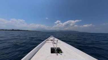 Okyanusta büyük dalgalar üzerinde, dağları olan tropik bir adaya doğru giden ahşap beyaz bir teknenin pruvasına yakın çekim. Okyanus yolculuğu, şnorkelle yüzme ve dalış turu. Tekne dalgalarda sallanıyor..