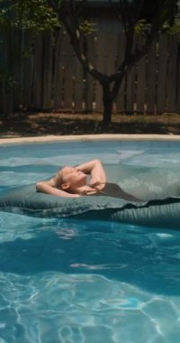 Genç bir kadın, gözleri kapalı bir havuzda yatağın üzerinde yüzüyor ve tropik bir adada tatilin tadını çıkarıyor. Kapsamlı otellerde rahatlama ve sağIık tedavileri. Spa tedavileri ve yüzme