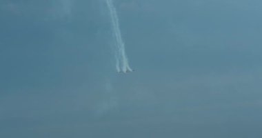 Bir hava gösterisinin yapıldığı mavi gökyüzünün altından görüntüyü al. Bir grup askeri uçak inanılmaz numaralar sergiliyor. Uçağın arkasında bir buhar şeridi var. Profesyonellerin aşırısı.