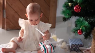 Beyaz elbiseli küçük bir kız sabah Noel ağacının yanında yere oturur ve Noel Baba 'nın ona verdiği hediyeleri açar. Ambalaj kağıdını yırttı. Sihirli bir tatil sabahı