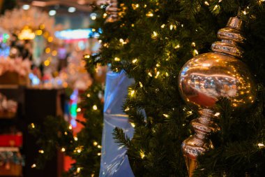 Bir alışveriş merkezinde duran süslemeleri olan bir Noel ağacının yakın çekimi. Ağaç altın toplar ve ışıklarla süslenmiş. Arka planda, Yeni Yıl dekorasyonları bulanık.