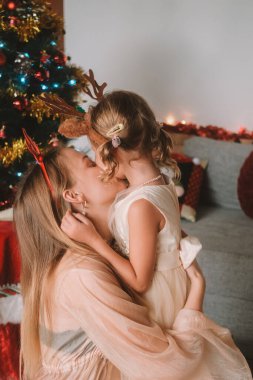 Genç bir kadın ve boynuzlu boynuzlu kızının portresi. Noel ağacına sarılıyorlar. Evin rahatlığında aile tatili. Aşk ve sevgi.