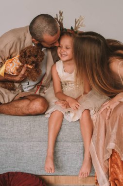 Aile Noel 'i Küçük bir kız, anne ve babasının arasında kucağında oyuncak bir kanişle oturuyor. Annem ve babam aynı anda kızlarını öpüyor, o da gülüyor ve mutlu oluyor..