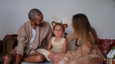 Aile Noel 'i Küçük bir kız, anne ve babasının arasında kucağında oyuncak bir kanişle oturuyor. Annem ve babam aynı anda kızlarını öpüyor, o da gülüyor ve mutlu oluyor..