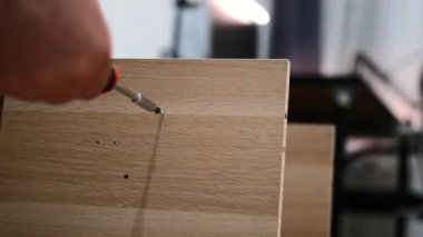 Oturma odasında dolap kuran ve vidaları vidalayan bir adamın ellerini kapatın. Ev tadilatı ve iç dekorasyon için yeni mobilyalar. Tamirci işini yapıyor. Yeni bir eve taşınıyorum..