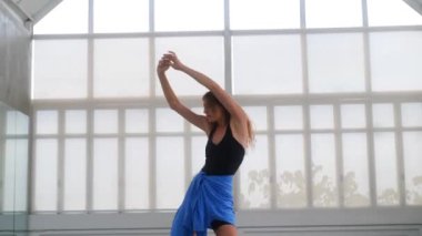 Parlak bir stüdyoda şehvetli çağdaş bir dans sergileyen bir kadının orta ölçekli görüntüsü. Hareketleri etkileyici. İzleyiciyi büyülerken kendine güvenini ve zarifliğini vurguluyor..