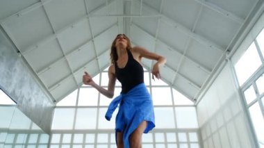 Parlak bir minimalist stüdyoda enerjik ve güçlü bir çağdaş dans gösterisi yapan bir kadın dansçının orta boy fotoğrafı. Hareketleri dinamik ve güç dolu..