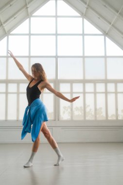 Bir kadın, geniş pencereli parlak bir stüdyoda çağdaş bir dans sergiliyor. Duruşu hareketi ve esnekliği vurguluyor, fitness, dans ve yaşam tarzı tasvirleri için ideal hale getiriyor..