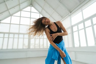 Parlak bir stüdyoda çağdaş bir dans gösterisi sırasında zarif bir şekilde kollarını ve başını hareket ettiren bir kadın dansçının yakın plan portresi. Onun ifadesi tutku ve zarafeti yansıtır..